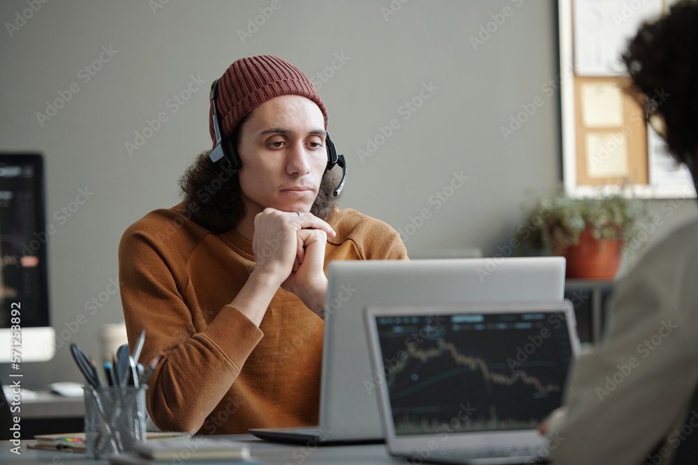 Aufkleber Young serious male IT support operator sitting by workplace in front of laptop and looking at camera while listening to online client