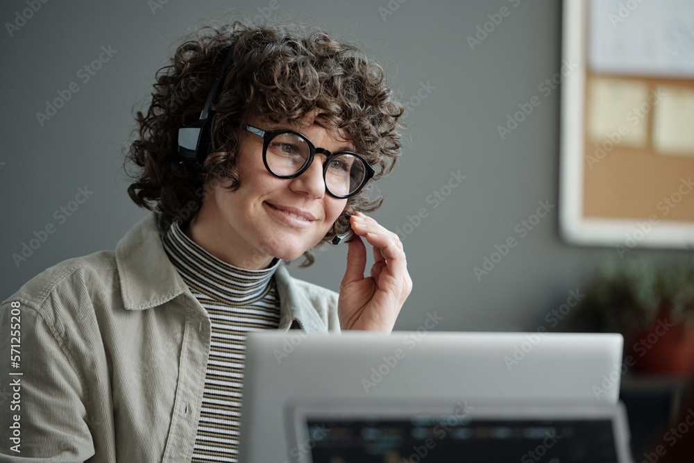 Aufkleber young smiling female it support engineer in headset looking at laptop screen and answering questions