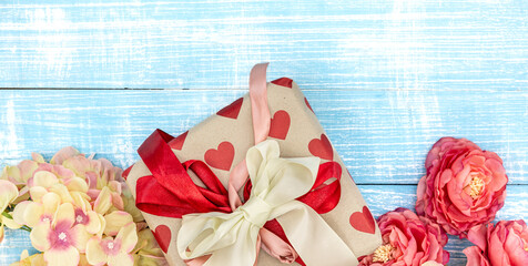 Spring background with flowers and a gift box on a blue background, top view.