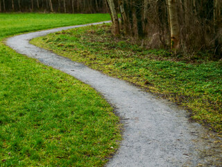 S shaped small foot path in a park by a trees and green grass lawn. Nobody.
