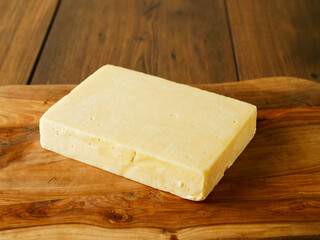 Uncut block of red cheddar on a wooden cutting board and table. Premium high quality dairy product...