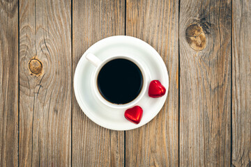 A cup of coffee and heart-shaped chocolates on a wooden background, top view.