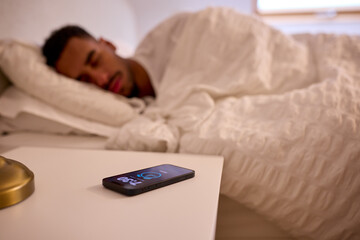 Fototapeta premium Man At Home Asleep In Bed With Alarm Going Off On Mobile Phone