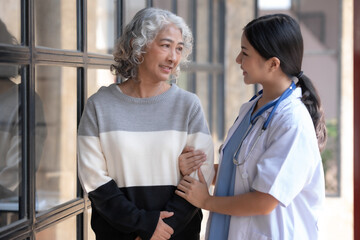 Asian female doctor or nurse gently guide and care for elderly patient at home, giving warm...