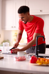 Man In Kitchen At Home Wearing Fitness Clothing Blending Fresh Ingredients For Healthy Drink