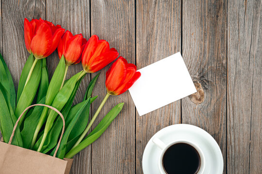Bouquet of red tulips, a cup of coffee and a blank sheet, space for text.