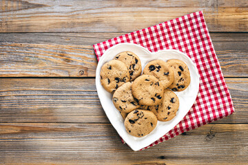 Heart shaped plate with chocolate chip cookies on wooden background, flat lay.