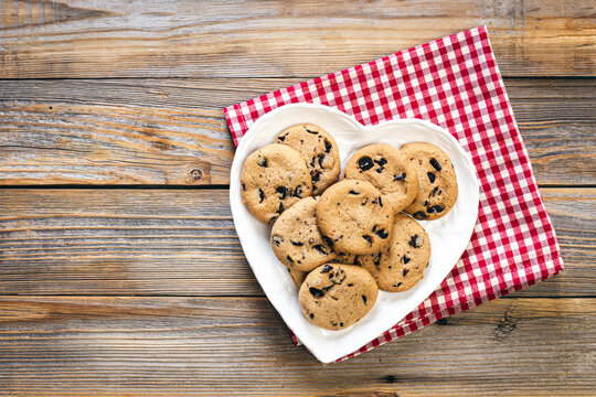 Heart shaped plate with chocolate chip cookies on wooden background, flat lay.