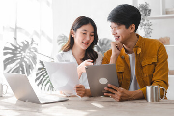 Asian couple husband and wife using laptop and paper bills at home use banking applications sit...