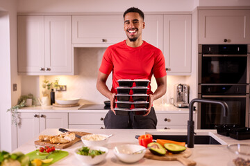 Portrait Of Man In Kitchen Wearing Fitness Clothing Making Batch Of Healthy Meals For Freezer