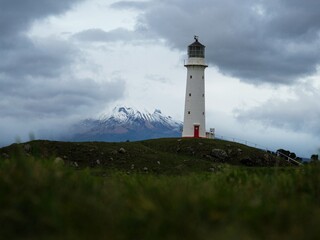 Fototapeta na wymiar Low angle grass shot of tall white Cape Egmont Lighthouse with Mount Taranki in background North Island New Zealand