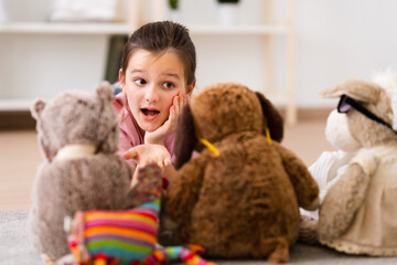 Little girl talking to fluffy toys lying down on floor