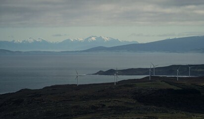 Oceanside clean green renewable energy windmill plant park with snow capped mountain in background,...