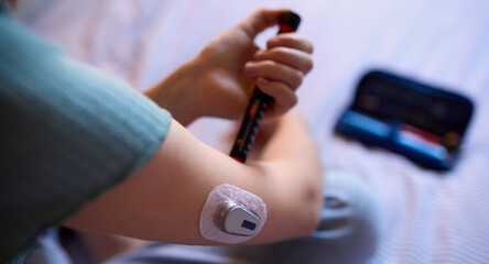 Obraz na płótnie Canvas Close Up Of Diabetic Girl On Bed In At Home Using Insulin Pen To Measure To Check Blood Sugar Level