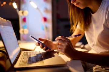 Fototapeta na wymiar Close Up Of Teenage Girl Studying At Home With Laptop And Mobile Phone In Bedroom Desk At Night