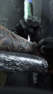 Vertical video process of tattoo artist making a tattoo on a male arm, professional tattooist with sterile tattoo machine and gloves with white ink. Soft light
