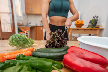 Athletic girl in sportswear cooking in a kitchen with fresh vegetables, vegan or vegetarian woman. Proper nutrition concept
