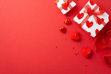 Valentine's Day concept. Top view photo of gift boxes ribbon heart shaped candles chocolate candies and sprinkles on isolated red background with empty space