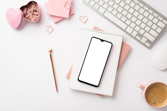 Valentine's Day concept. Top view photo of smartphone over diaries pen keyboard sticky note paper heart shaped clips holder and mug of coffee on isolated white background with blank space