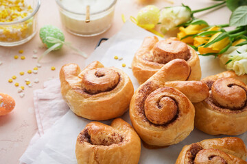 Easter breakfast Holliday concept. Easter bunny buns rolls with cinnamon made from yeast dough with orange glaze, easter decorations, colored eggs on pink spring background. Easter Holliday card.