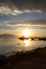 Boat on the beach of a lake at sunset with a dock in the background