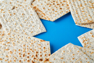 Passover celebration concept. Blue Star of David made from matzah, white and yellow roses, kippah and walnut on bluebackground. Traditional ritual Jewish Passover food. Pesach Jewish holiday. Mock up