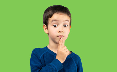 Pensive child looks away at copy space thinking isolated on a green background, funny kid lips hold...