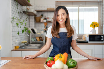 Pretty Asian woman preparing healthy breakfast at home in modern and beautiful kitchen, smiling brightly.