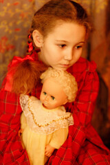 a girl in a red dress with an old doll, filmed in a studio in daylight