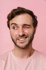 Fototapeta premium Cheerful man winking and looking aside while posing isolated over pink wall