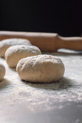 raw bread with rolling pin and scattered flour on black table