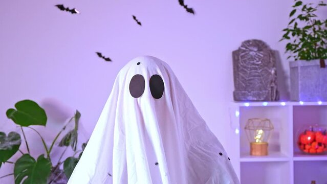 White ghost costume for Halloween party with neon lights in the background. The ghost is celebrating Halloween. A ghost at a confetti party. Portrait of a ghost. The monster is celebrating Halloween.