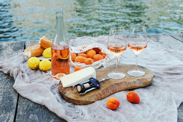 Rose wine, fruits and snacks on the wooden pier during picturesque picnic on the wooden dock