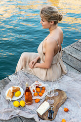 Lovely young woman picturesque picnic on the wooden gondola dock with rose wine, fruits and snack on wooden pier © blackday