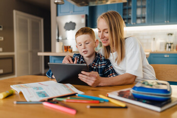 Cheerful mom with her son using tablet computer while sitting in kitchen