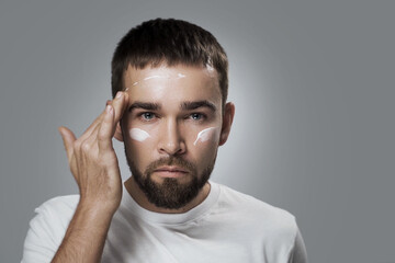 Young man is applying moisturizing cream on his face