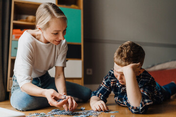 Smiling mom and her son playing with puzzle pieces while sitting on floor