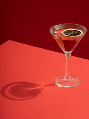 Red cocktail drink in martini glass with dried lemon slice on a red table and red background. Hard...