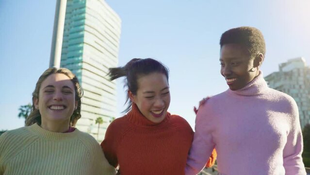 Three female friends walking arm in arm outdoors in the city during a sunny day. Leisure and freedom concept. High quality 4k footage
