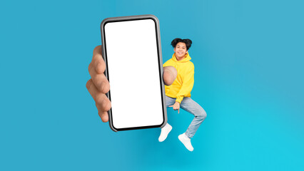 Fototapeta na wymiar Asian Teenager Boy Showing Large Cellphone Screen Jumping, Blue Background