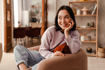 Beautiful asian woman smiling and looking away while sitting at home
