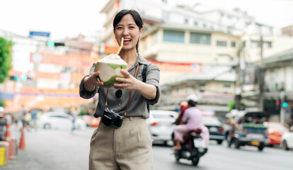 Happy young Asian woman backpack traveler drinking a coconut juice at China town street food market in Bangkok, Thailand. Traveler checking out side streets. 