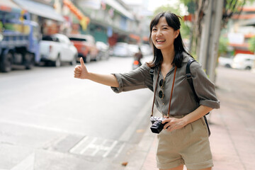 Smiling young Asian woman traveler hitchhiking on a road in the city. Life is a journey concept.