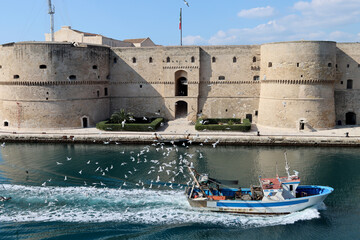 Aragonese Castle of Taranto with fishing boat returning to the port surrounded by dozens of...