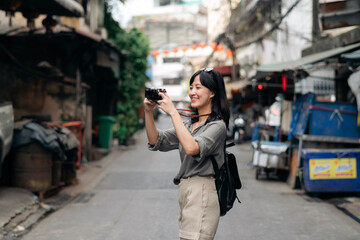 Fototapeta premium Young Asian woman backpack traveler using digital compact camera, enjoying street cultural local place and smile. Traveler checking out side streets. 