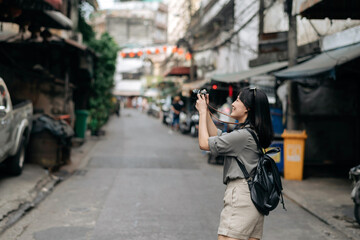 Young Asian woman backpack traveler using digital compact camera, enjoying street cultural local place and smile. Traveler checking out side streets. 