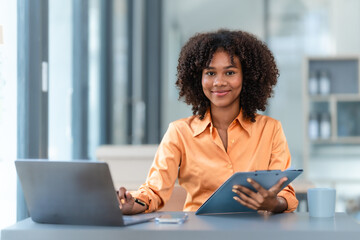 Using laptop computer, Young pretty african american business woman bookkeepers working with balance sheet yearly reports to calculate tax and online consult in modern office.