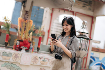 Young Asian woman backpack traveler using mobile phone, enjoying street cultural local place. Traveler checking out side streets.