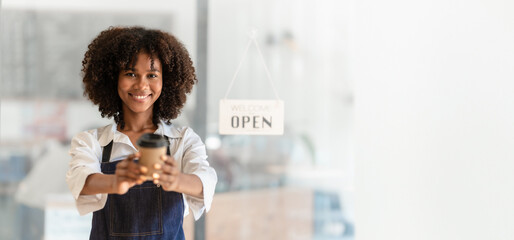 Attractive African American barista woman in apron feeling happy while working at coffee and bakery shop.