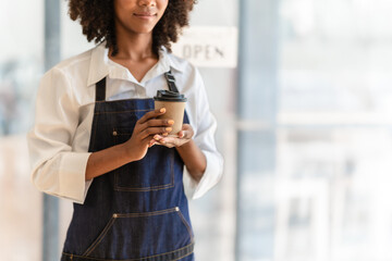 Attractive African American barista woman in apron feeling happy while working at coffee and bakery shop.